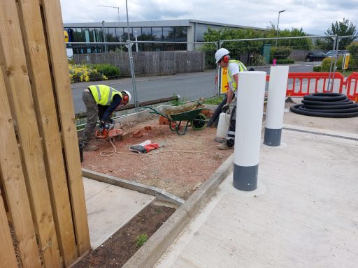 Two workers in high-vis vests digging a garden area near a construction site.