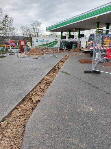 Uneven ground at a gas station with construction barriers and machinery in the background.