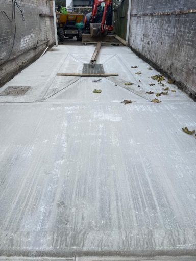 Freshly laid concrete surface with light debris and machinery in the background.